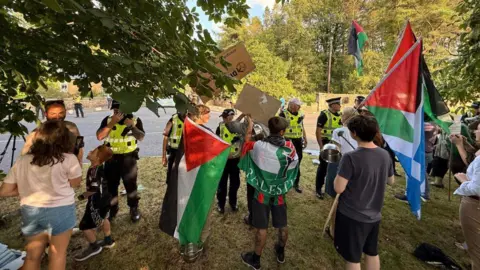 PA Media A group of protesters, many waving Palestine flags standing behind a row of police officers