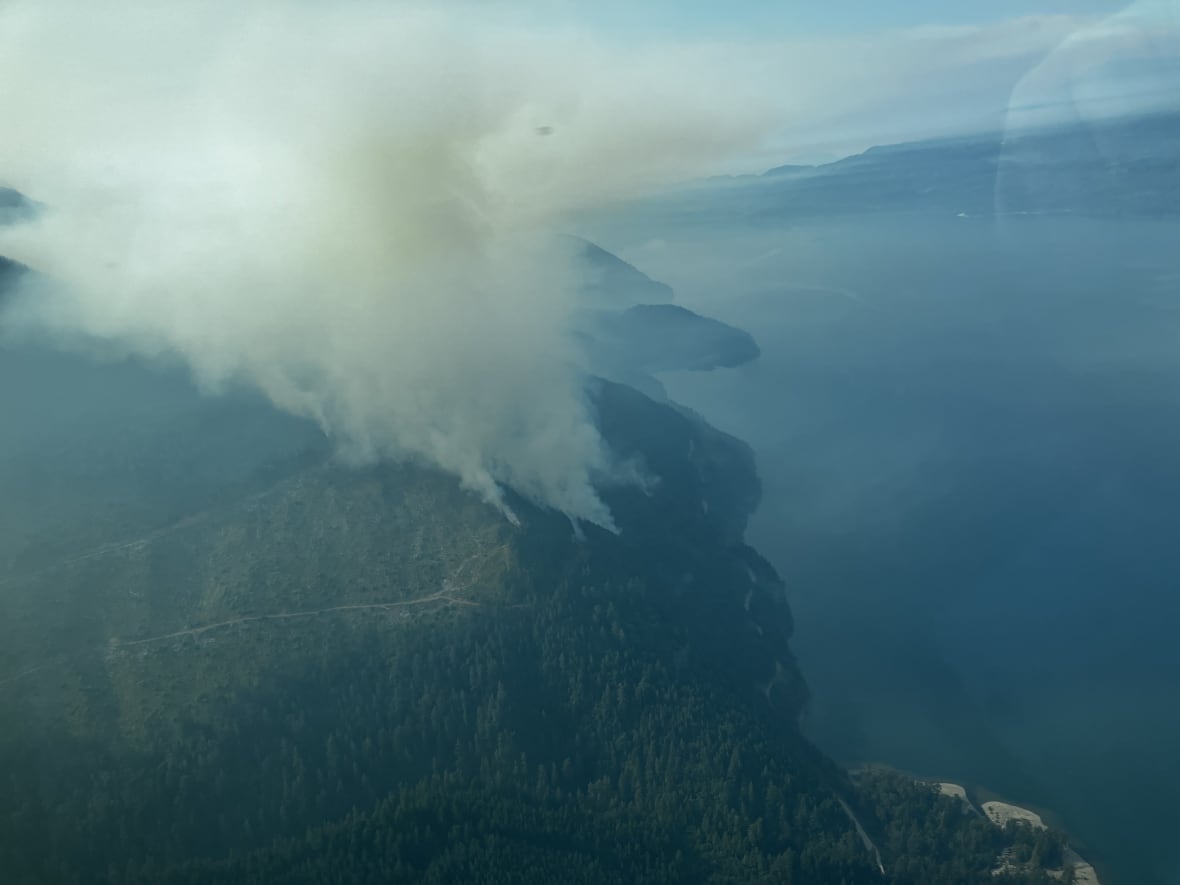 Smoke arises from a hill near a picturesque lake.