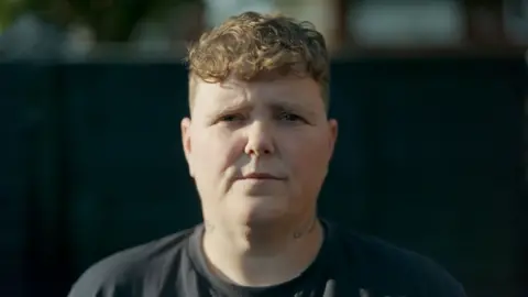BBC A close-up of Amy Hodgkinson-Hedgecox, a woman with short brown hair and brown eyes, looking to straight at the camera with the background blurred