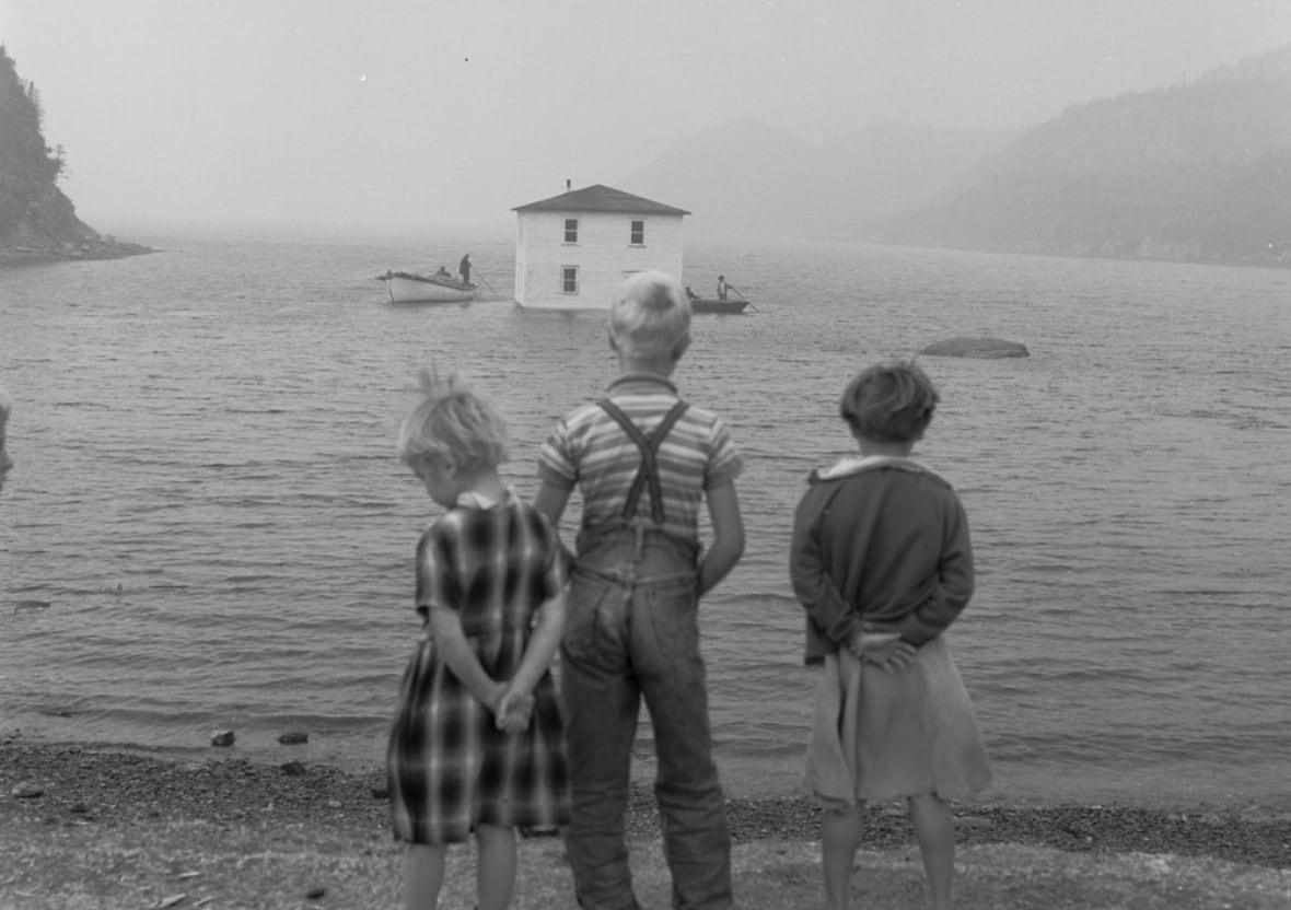 Black and white photo of three children standing on a beach.