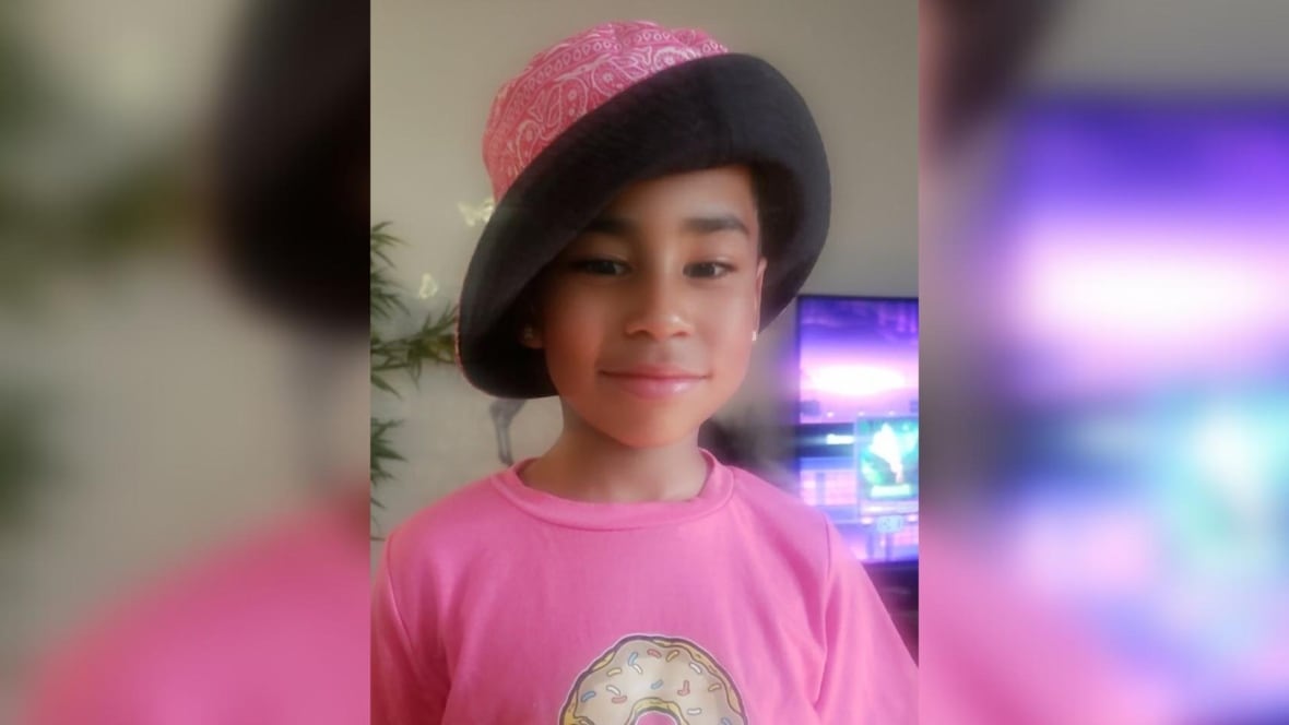 Photo of a boy in a pink t shirt and black and pink hat. 
