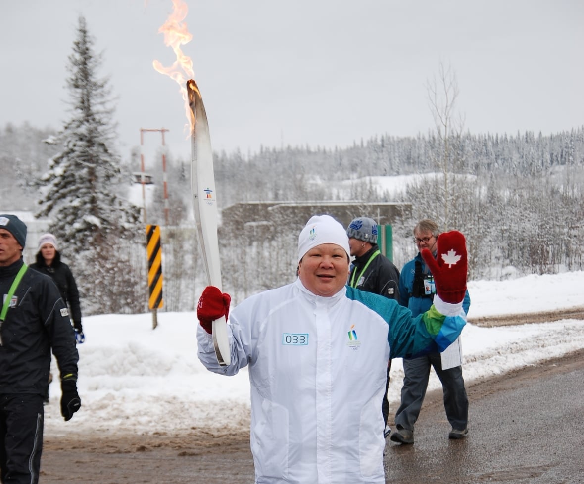 A woman in white holds a stylized Olympic torch.