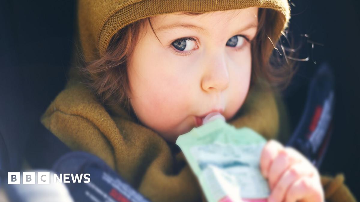 A stock image of a young child with brown hair sucking on a pouch of food
