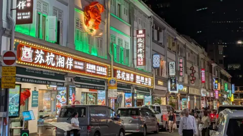 A row of Chinese restaurants, many fronted by bright neon signboards, along Liang Seah Street in central Singapore