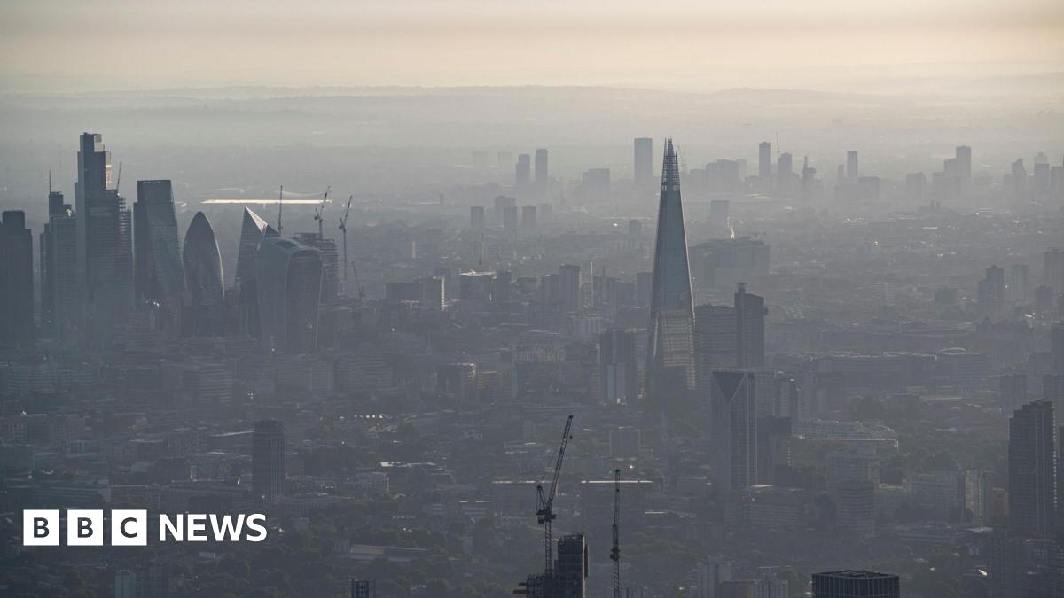 A hazy aerial view of central London, with the Shard and other skyscrapers partially obscured by a haze under a pale sky.