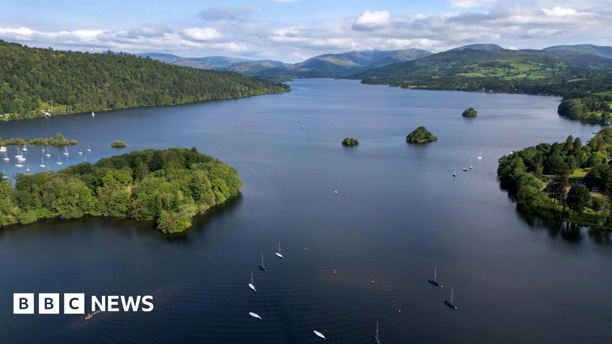 A drone view of Lake Windermere. Boats can be seen o the lake and trees and fields line the lake shoreline.