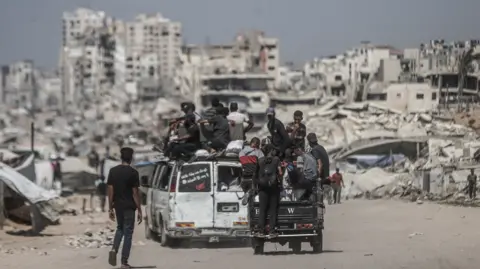 Getty Images Residents in Gaza City, with buildings destroyed by the Israeli attacks in the background, 24 August