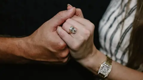 @TaylorSwift/Instagram Kelce's hand holding Swift's hand, and her ring, which is big and sparkly, is visible on her ring finger. She also wears a gold watch with diamonds.