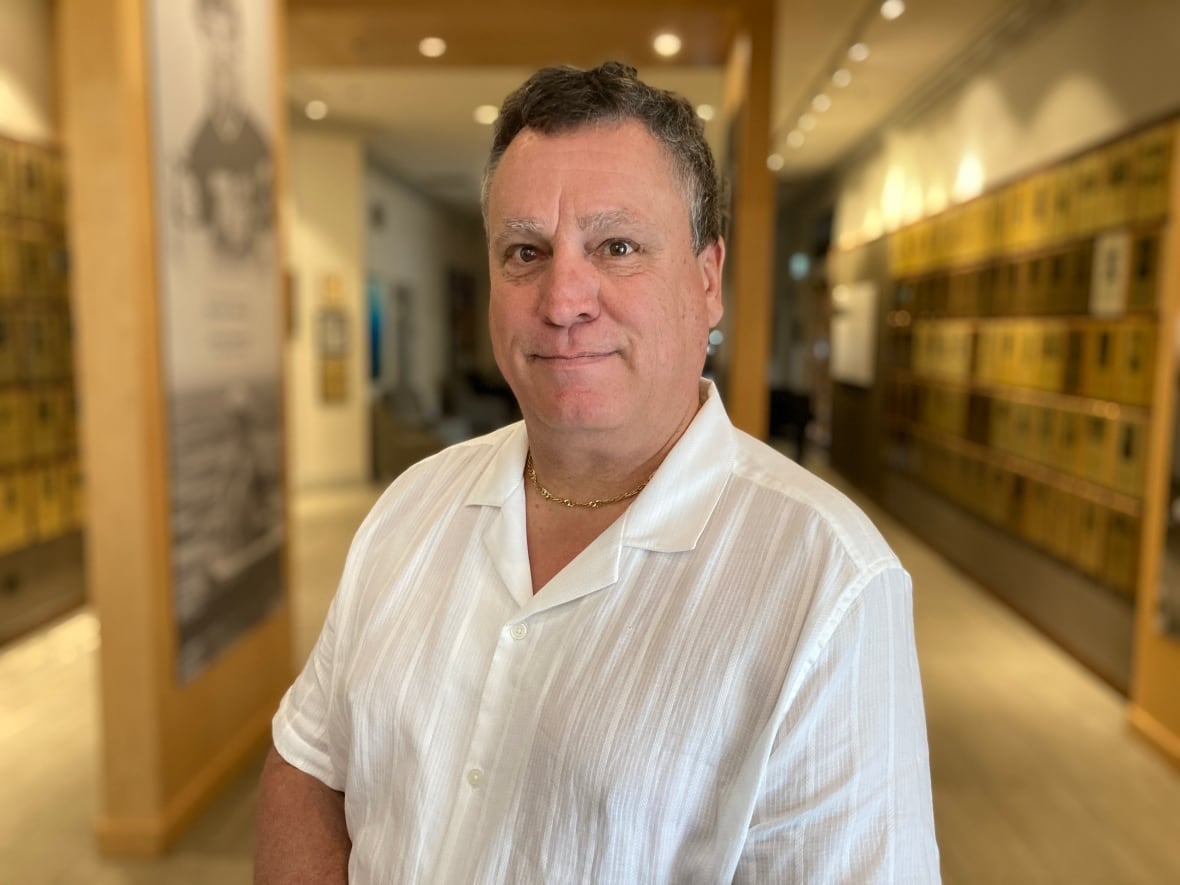 A man with thin grey hair and a white polo looks into the camera.