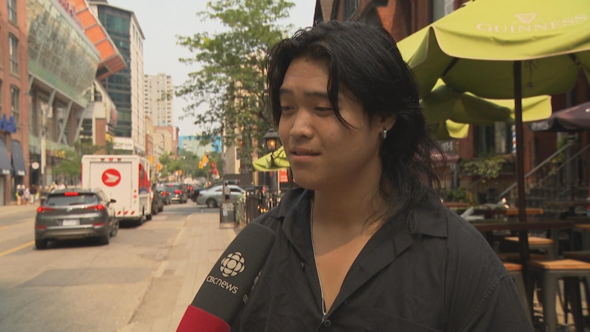 Photo of a man wearing a black shirt speaking into a microphone outside on a downtown Toronto street
