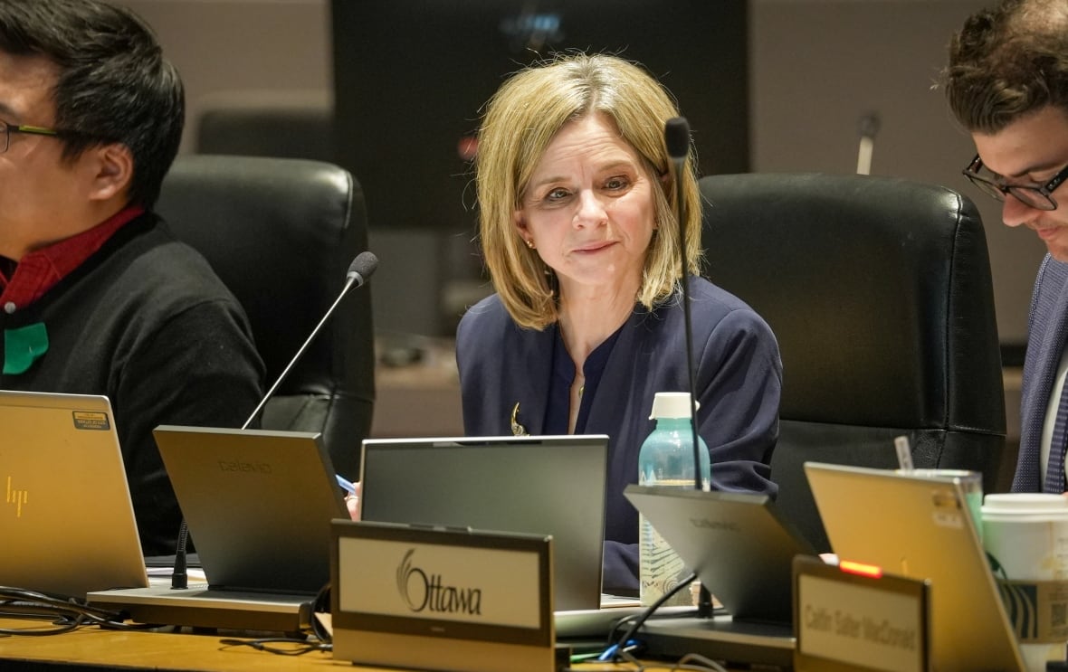 A woman with blonde hair sits in front of a thin microphone