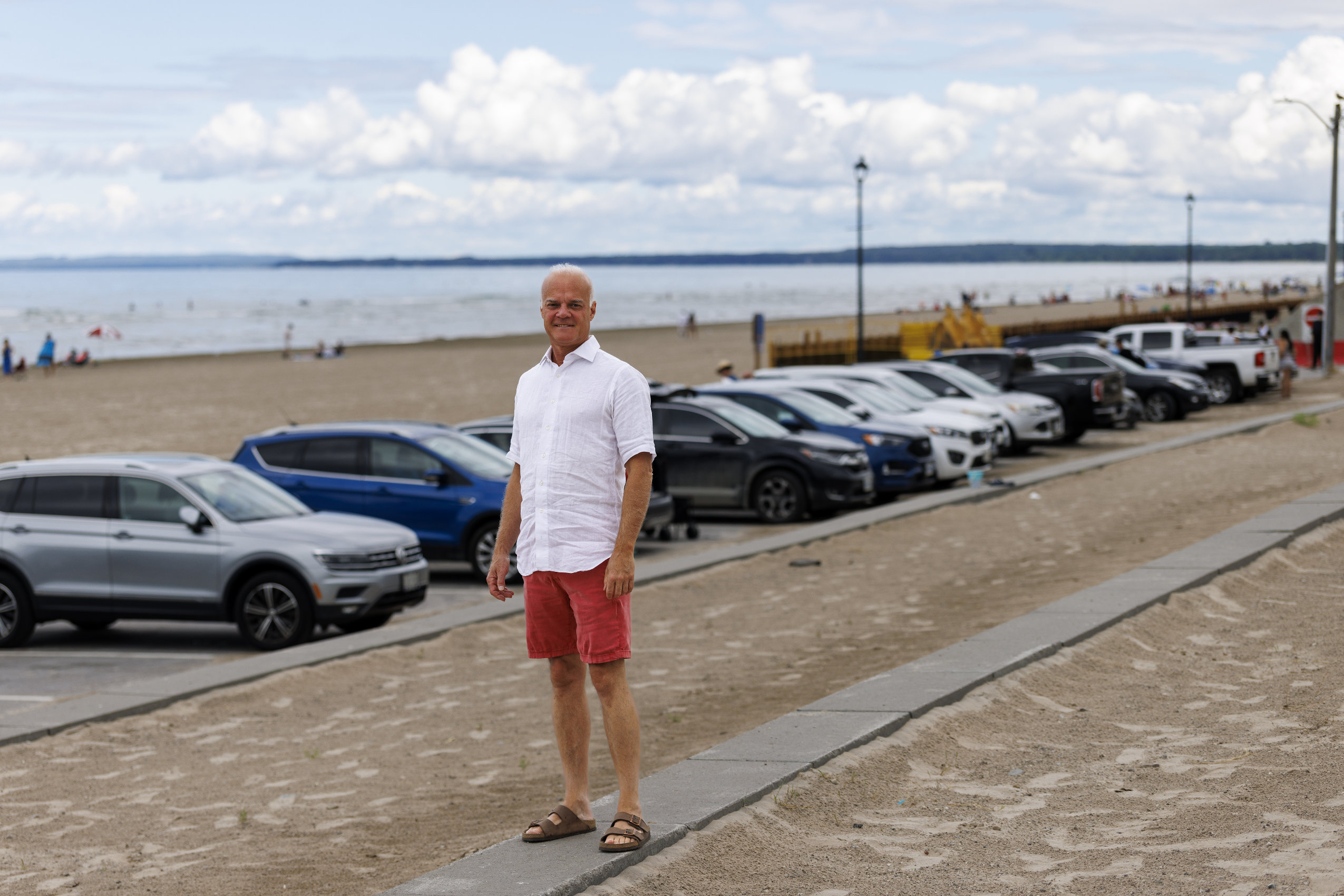 Ted Crysler, a longtime resident of Wasaga Beach, poses for a photo with a row of cars and the iconic beach behind him.