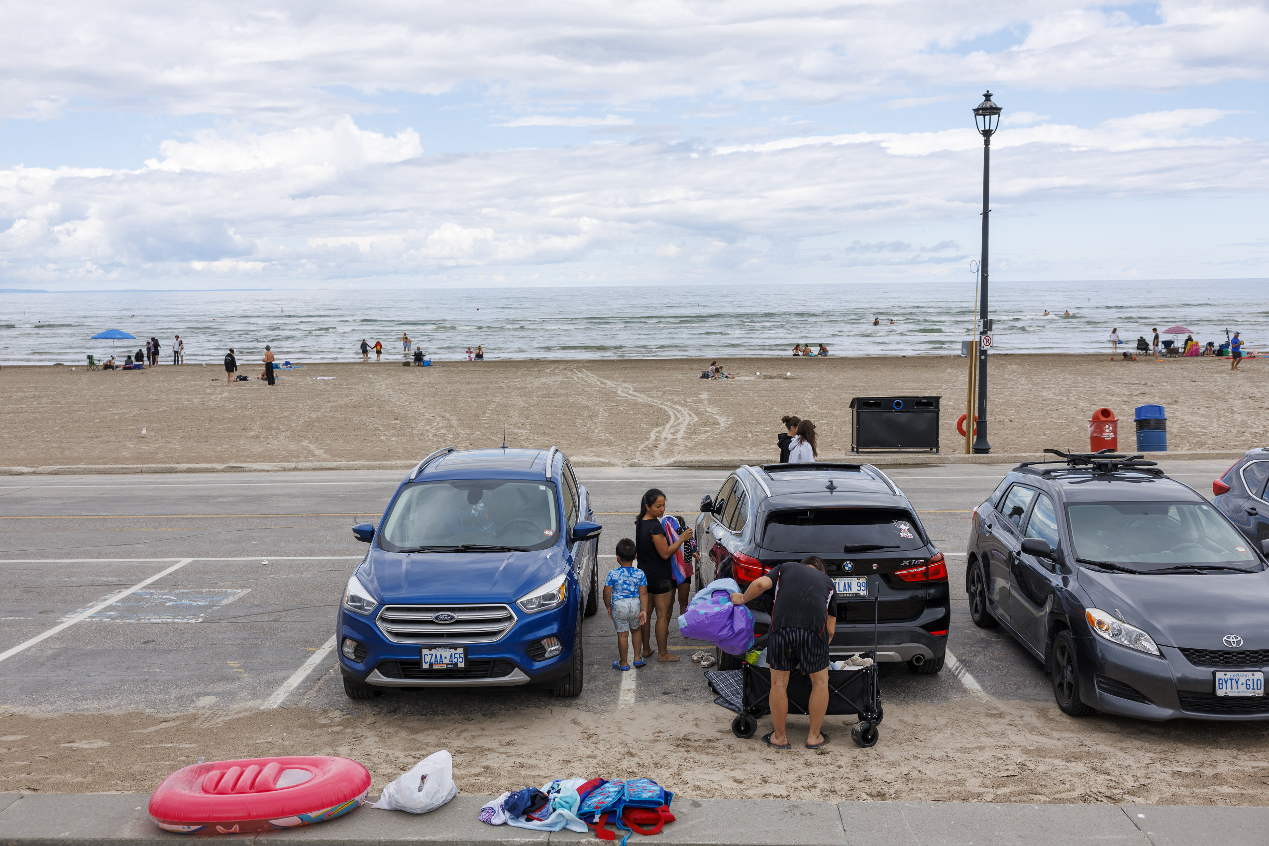 Two adults and two children pack their beach gear beside a vehicle, with Wasaga Beach in the background.