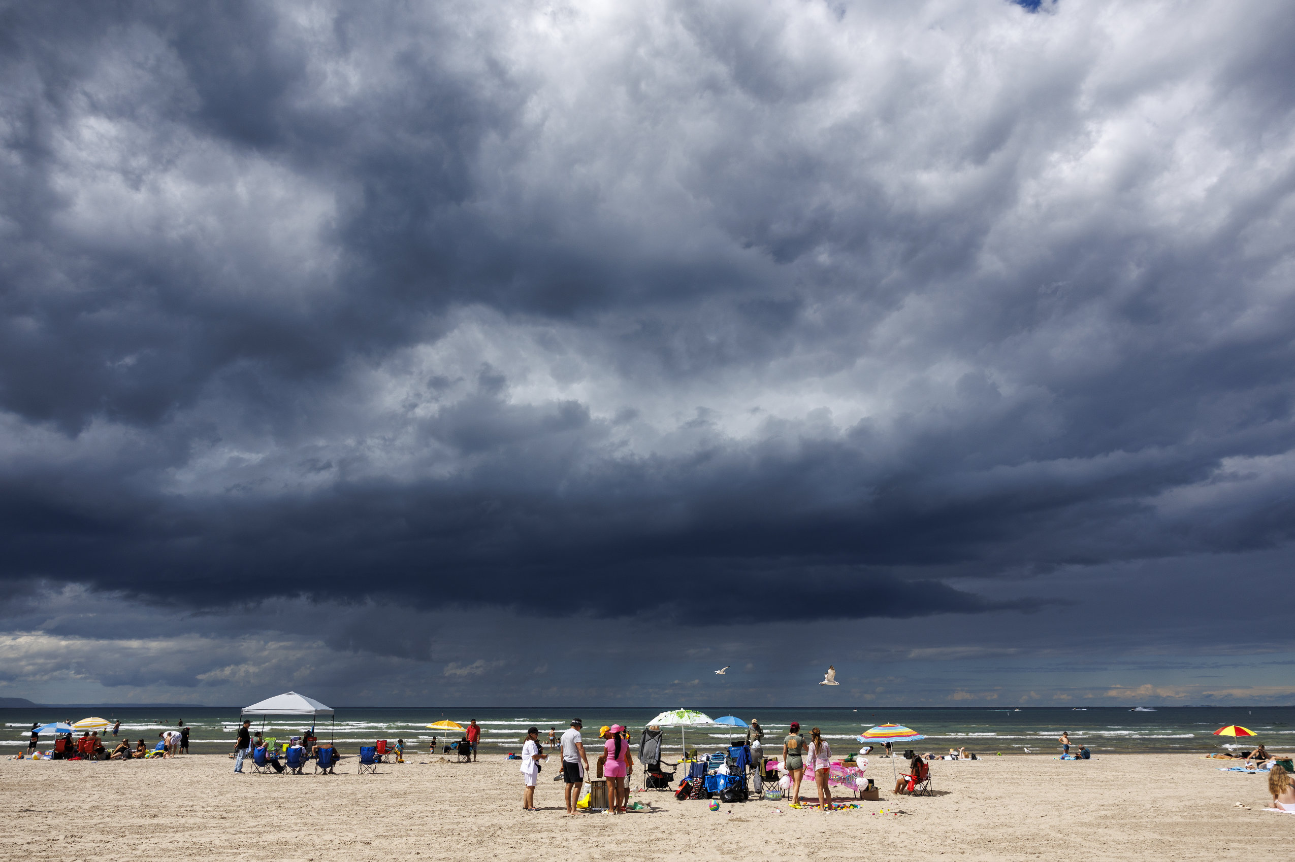 Visitors to Wasaga Beach are seen from behind. They are dwarfed by a dramatic and imposing cloudy sky.