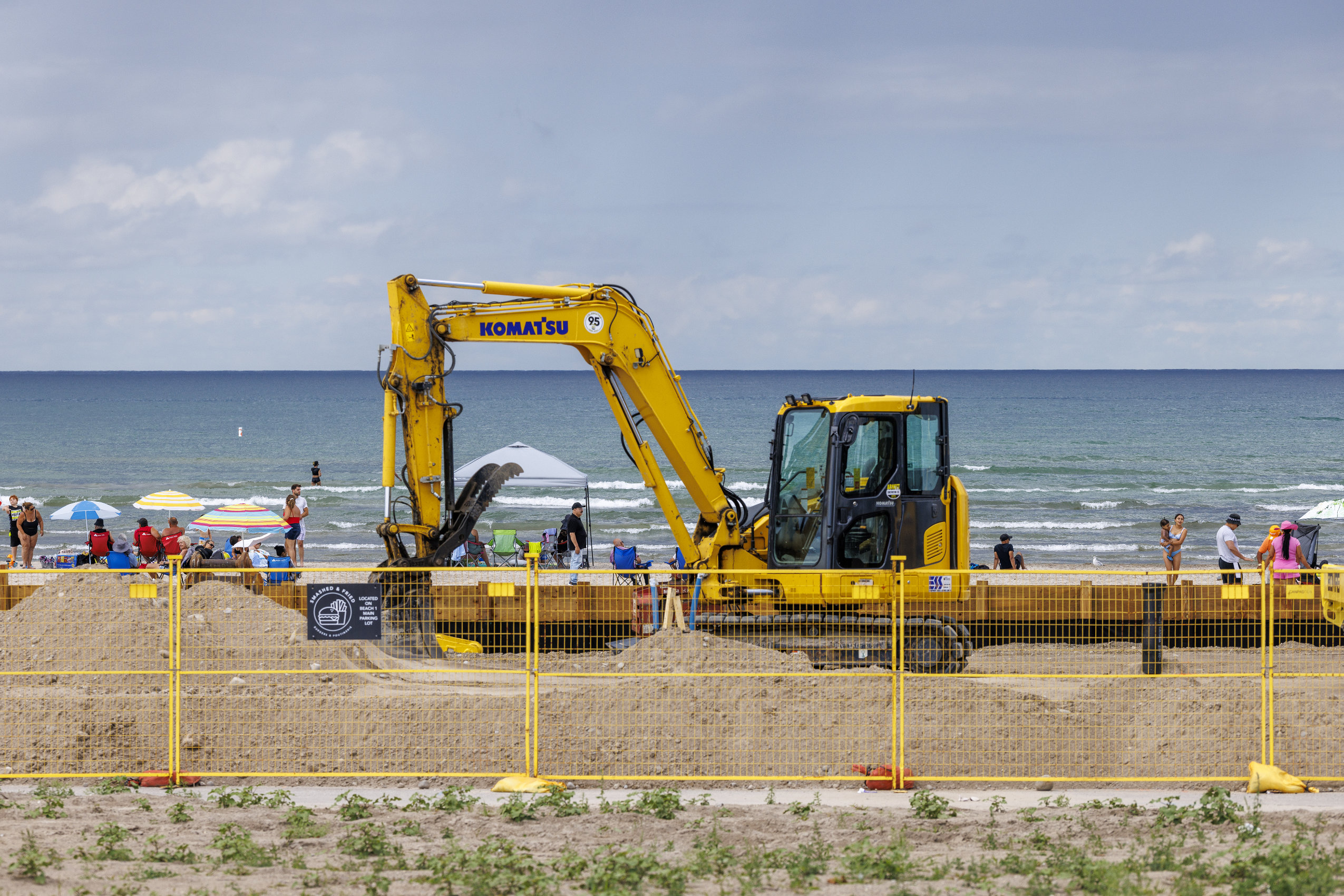 A backhoe and a yellow construction fence block access to Wasaga Beach and Lake Huron, which are seen in the background.