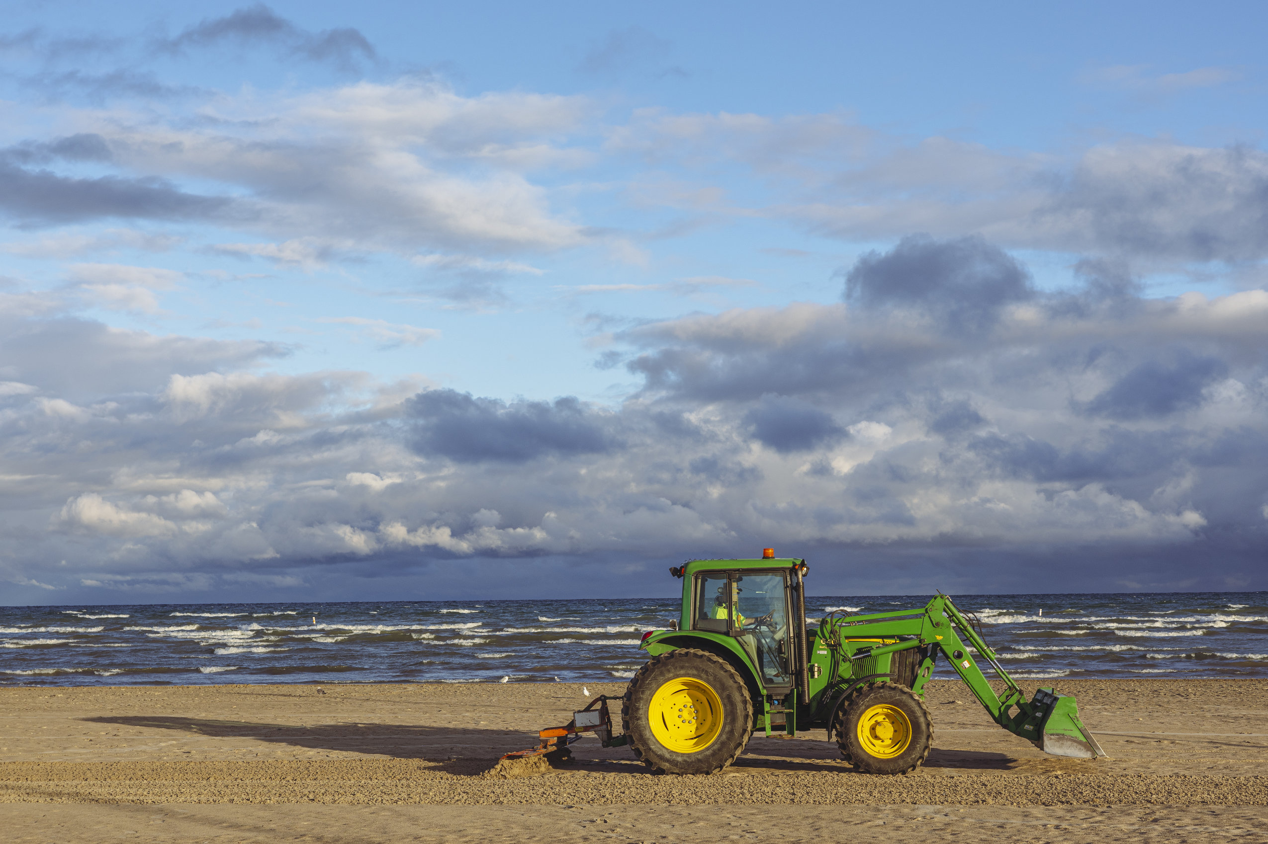 A green tractor drives along Wasaga Beach raking the sand.