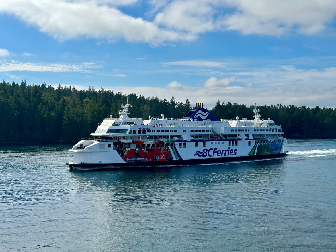 A large passenger ship sails through the water, with trees and blue sky behind it. 
