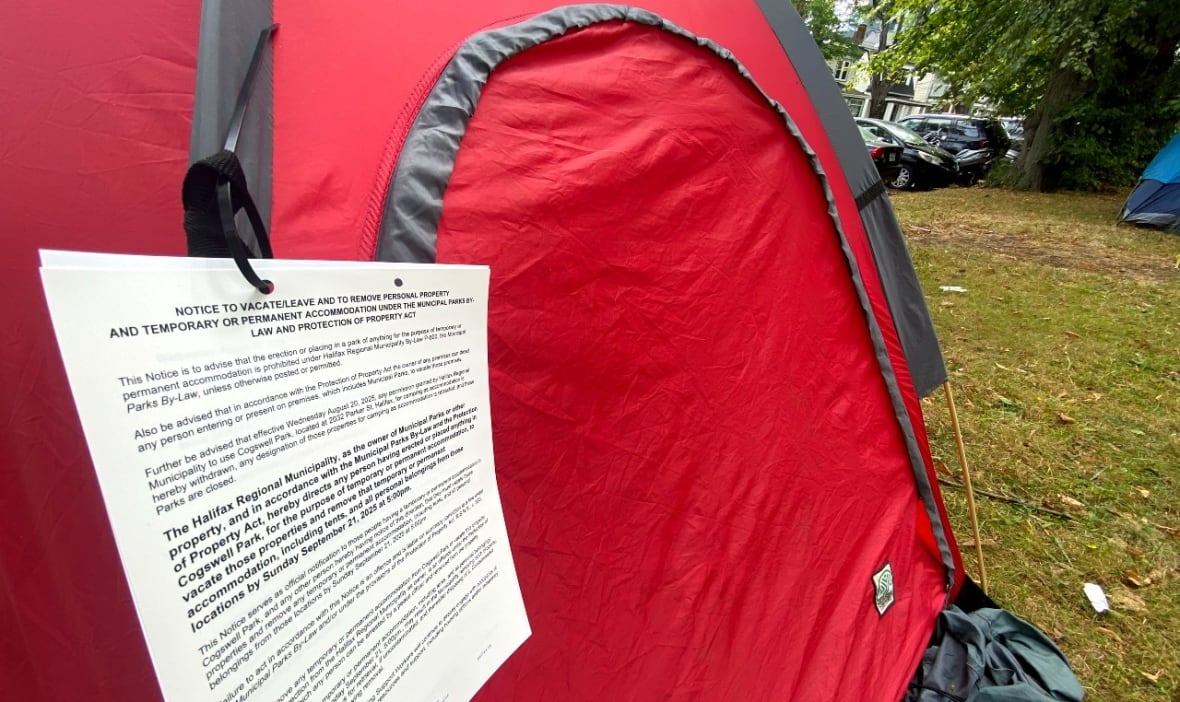 A red tent is seen sitting in a park, with pages of paper tied to its front zipper