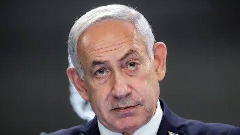 ABIR SULTAN/POOL/AFP via Getty Images Headshot of Israeli Prime Minister Benjamin Netanyahu staring ahead wearing a dark suit.