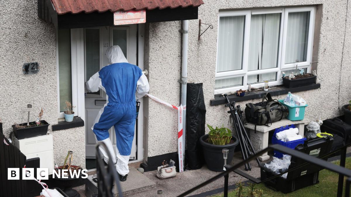 An individual in a forensic protective suit is walking into a property