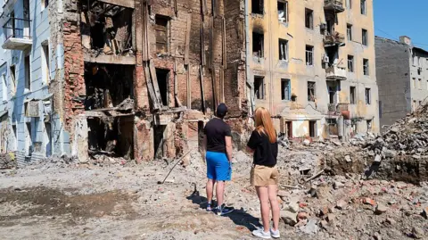 Getty Images Residents step out of their car to take in the devastation of residential buildings bombed by Russian forces on August 10, 2025 in Kramatorsk, Ukraine