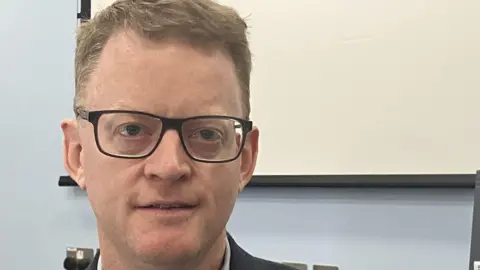 Professor Chris Fox at Nottingham City Hospital's haematology unit. Wearing glasses he is looking into the camera.  