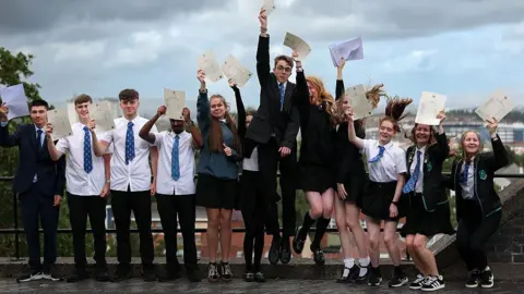 Getty Images Students smiling and jumping holding their a-level results 