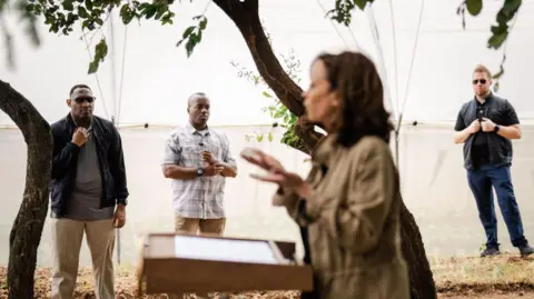 Getty Images Kamala Harris at a podium with three Secret Service agents in the background during a trip to Zambia in 2023. 