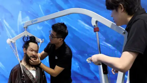 Reuters Staff members move a humanoid robot portraying emperor Qin Shi Huang from the Qin dynasty, which fell to the floor during an organised media tour to Robot Mall, a store selling humanoid and other robots, in Beijing, China August 6, 2025.