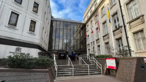 Simon Dedman/BBC Steps leading to Essex County Council's offices in Chelmsford. The large building is tall and made of cream bricks. It has a tall glass facade in the middle and several flags - including the Union Jack and St George's Cross - are flown on poles outside.