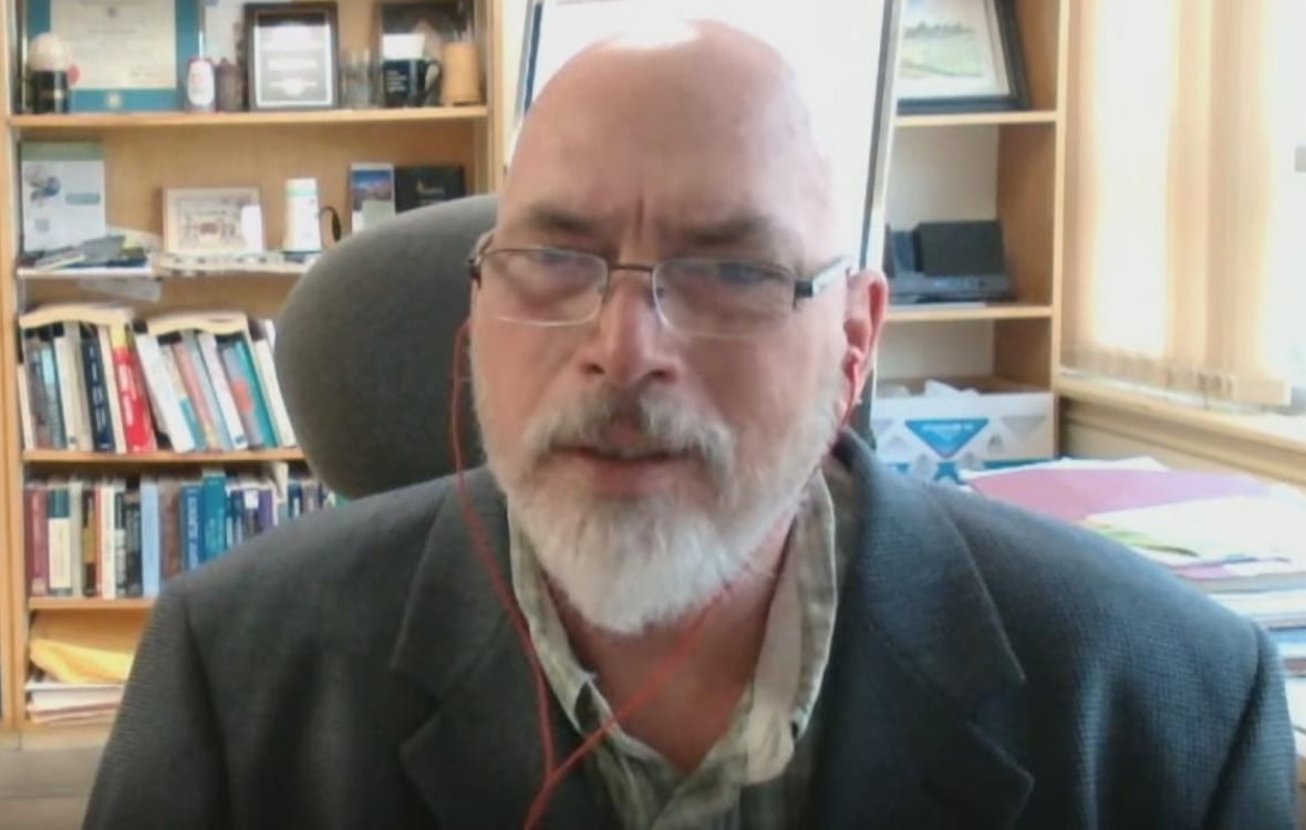 Derek Brewin sits in his book-laden office.