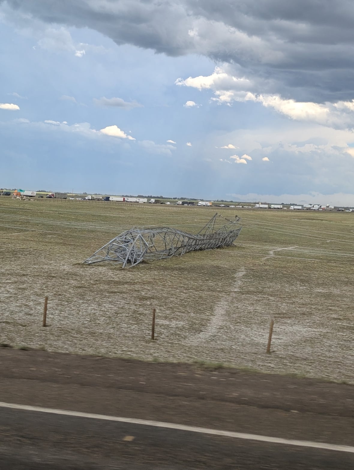 Downed power lines are seen in a field with stormy skies looming overhead.