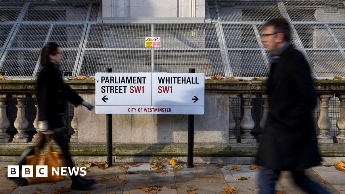Man and woman in winter coats walk past two road signs pointing to Parliament Street W1 in one direction and Whitehall SW1 in the other direction