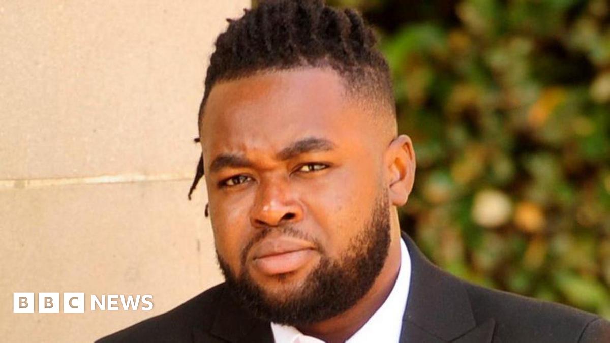 A man with a beard and dark hair, closely cropped at the sides, wearing a suit, pictured outside a court