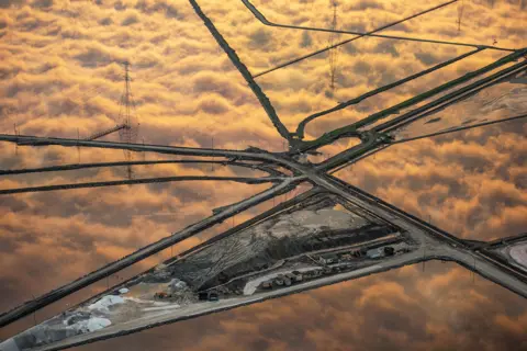 Jassen Todorov Golden-hued clouds are reflected perfectly in the grid-like pattern of salt ponds. The ponds stretch across the landscape, creating a patchwork of shimmering water and earth dividers. 
