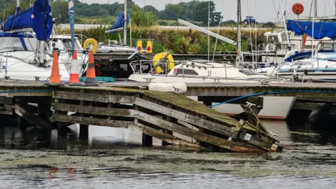 Lough Neagh Sailing Club Boats parked up at Kinnego Marina, with weeds gathered on top of the water. 