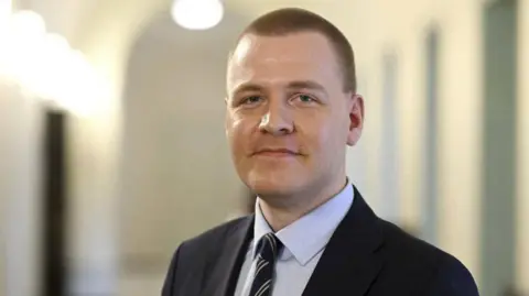 Reuters Eemeli Peltonen has short, light brown shaved hair and is wearing a suit. He is looking straight into the camera and smiling slightly.