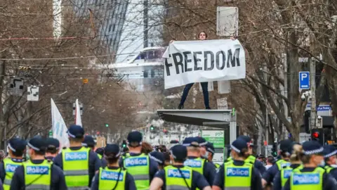 Getty Images A man holds a banner reading "Freedom" atop a tram stop during an anti-lockdown protest in Victoria in 2021