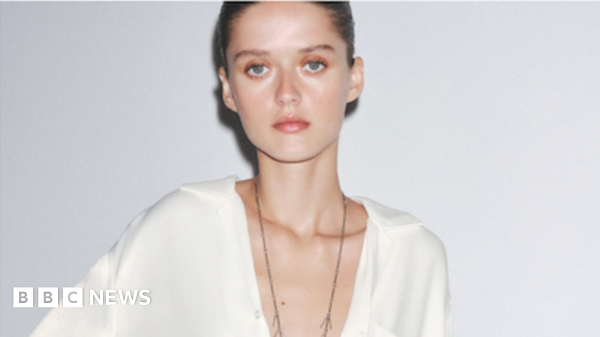 A pale model poses in a white Zara shirt staring at the camera with a blank expression and the low cut design of the top shows her protruding collarbones