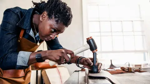 Getty Images Stock photo shows a maker hammering away at a piece of leather in a workshop.