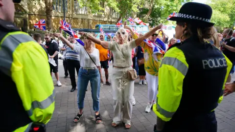 PA Media A group of anti-immigration protesters waving Union flags walk down a Bristol city centre street as police, with their backs to the camera, watch on