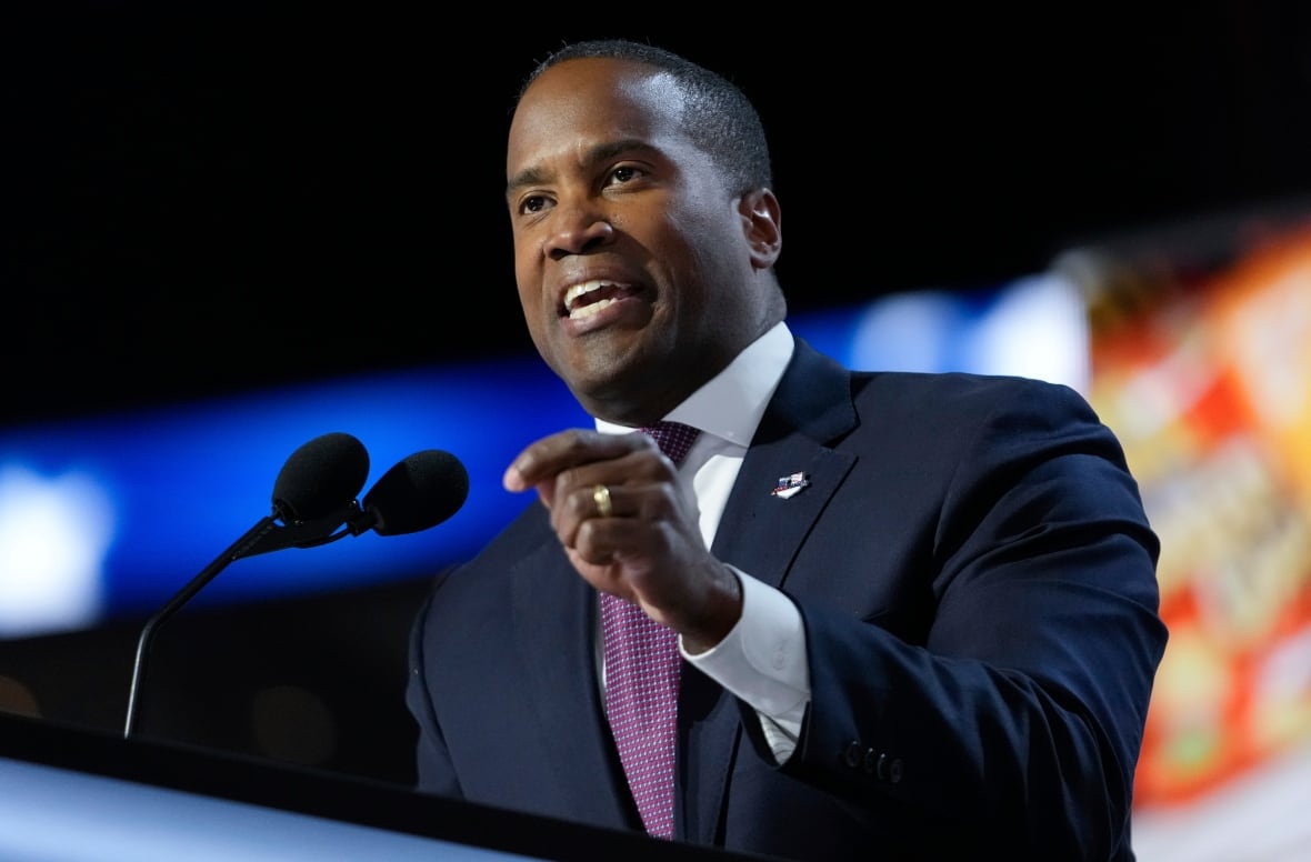 A man in a suit speaks into a microphone at a podium