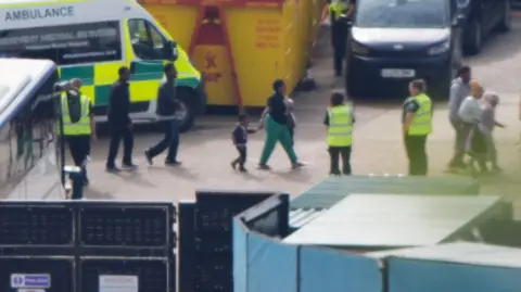 PA Media A small group of migrants - including children - being led by immigration officials on a tarmac at the Port of Dover on Saturday