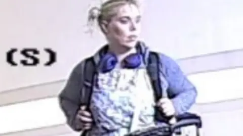Police handout Footage captures Betro possibly in a shop with baggage. She has headphones on over a blue jacket and patterned dress.
