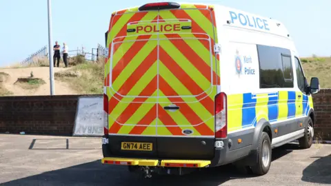 UKNIP A Kent Police van parked in a car park. In the background, police officers stand on a footpath.