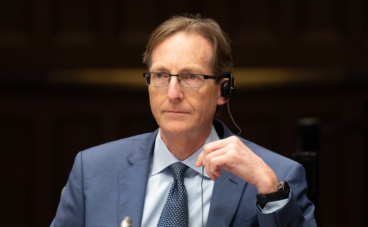 A man in a suit with an earpiece looks forward.