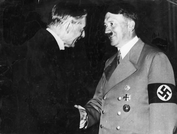 Two men shaking hands; one wearing a military uniform with a Nazi swastika on an armband.