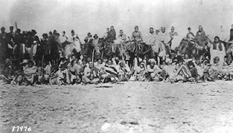 A grainy, black-and-white image of hundreds of people on what appears to be barren land.