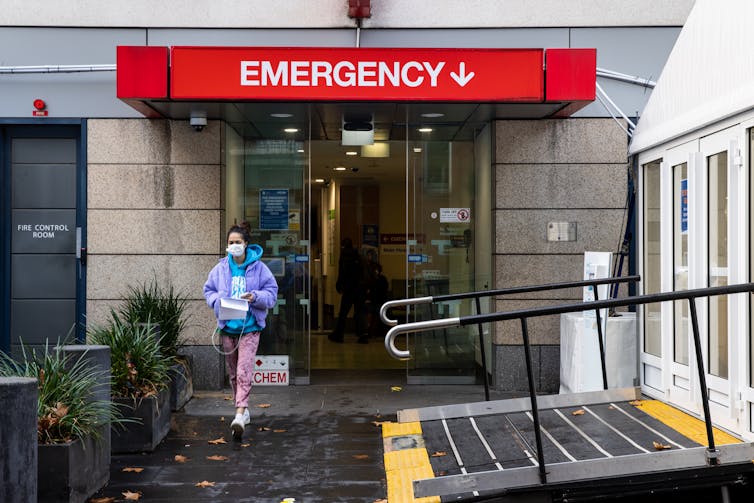 A woman wearing a mask walks out of a hospital.