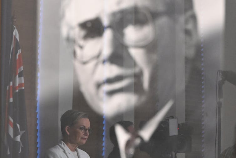 Sussan Ley gives a speech within the reflection of John Howard's portrait